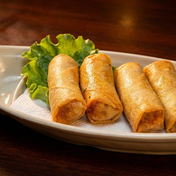 Four golden-brown spring rolls on a white boat-shaped plate with a lettuce leaf.