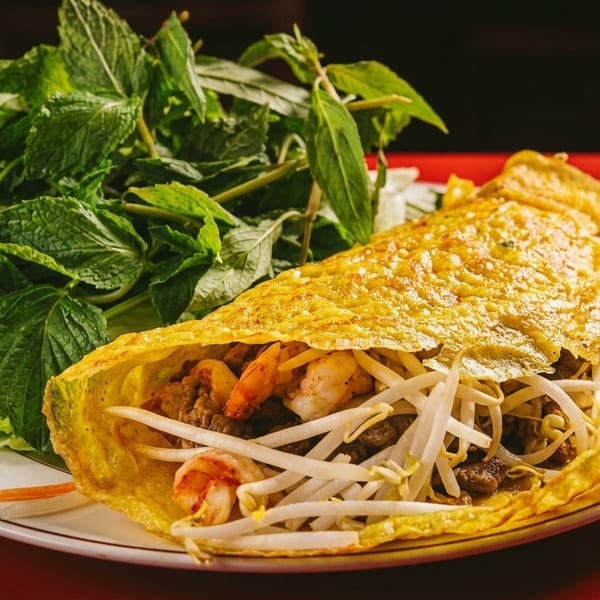 A Vietnamese bánh xèo pancake filled with shrimp, beef, and bean sprouts, served with fresh herbs.