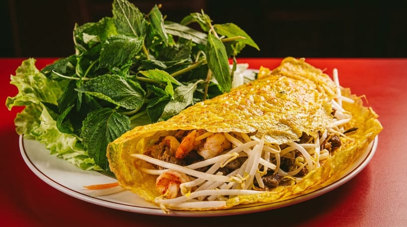 A Vietnamese bánh xèo pancake filled with shrimp, beef, and bean sprouts, served with fresh herbs.
