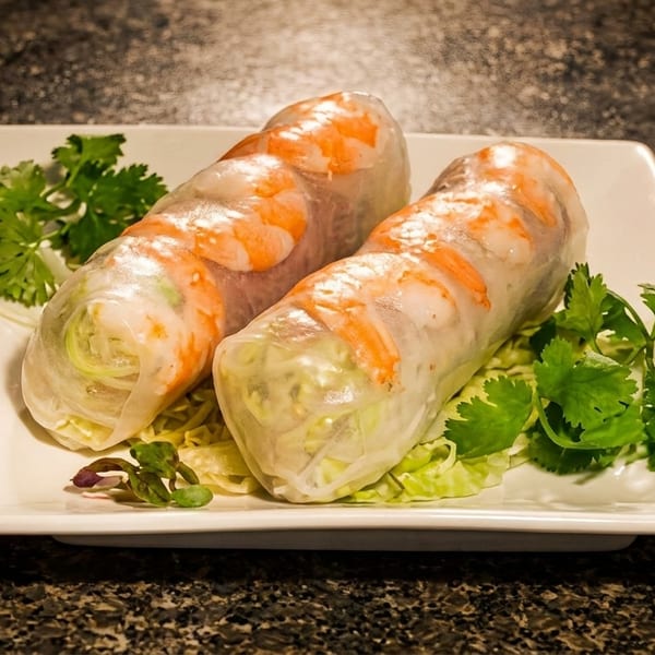 Two fresh spring rolls with shrimp and vegetables on a white rectangular plate with cilantro.