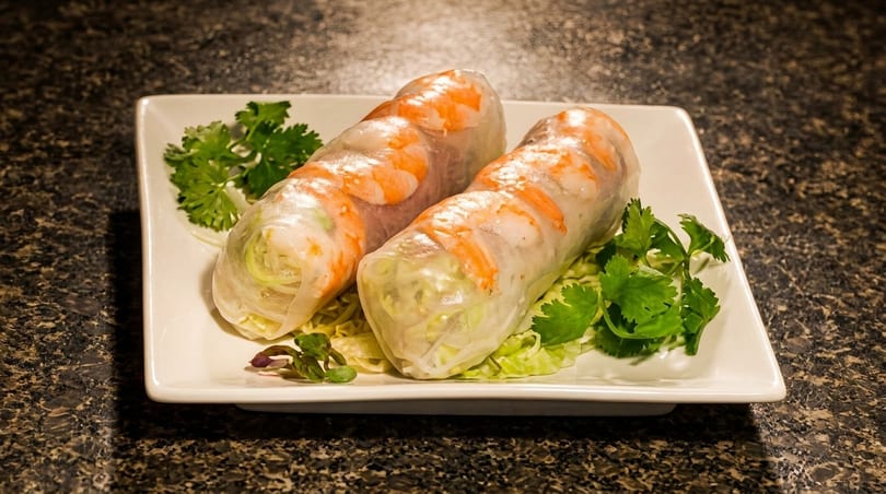 Two fresh spring rolls with shrimp and vegetables on a white rectangular plate with cilantro.
